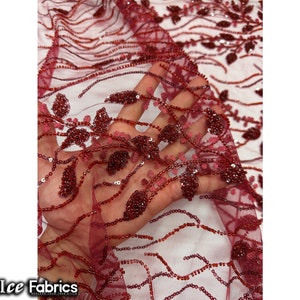 Puede incluir: Tela de encaje de color burdeos con cuentas y un dise&ntilde;o floral. La tela es transparente y tiene una textura delicada.