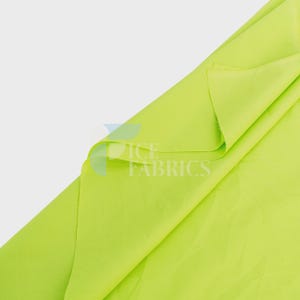 May include: A vibrant lime green fabric folded to display its smooth, matte texture. The material features a consistent, solid color throughout, with a semi-translucent watermark logo reading ICE FABRICS overlaid on the center of the textile.
