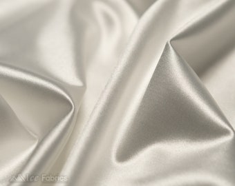 Könnte beinhalten: Ein Stück einfarbiger, weißer Satin-Stoff mit einer glatten, glänzenden Oberfläche und einem hochglänzenden Finish. Das Material ist in weichen, fließenden Falten drapiert, die tiefe Schatten und helle Glanzlichter auf der reflektierenden Oberfläche erzeugen.
