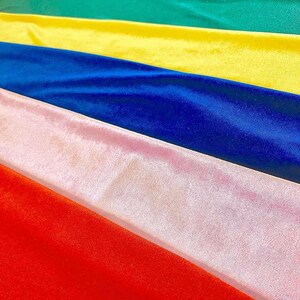 May include: A stack of six velvet fabric swatches in different colors, including red, pink, blue, yellow, and green.
