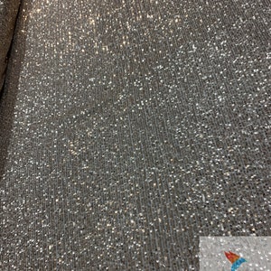 May include: A close-up of a gold sequined fabric with a subtle shimmer. The sequins are small and densely packed, creating a luxurious and glamorous look.