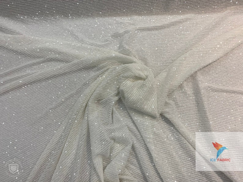 May include: White fabric with a subtle shimmer, featuring a textured, ribbed pattern. The fabric is draped and folded, showcasing its soft and flowing texture.