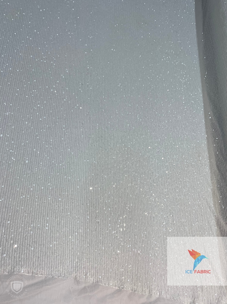 May include: White fabric with a subtle sparkle and a ribbed texture. The fabric is rolled up and the edge of the roll is visible. The text "ICE FABRIC" is visible in the bottom right corner of the image.