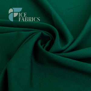 Peut inclure: Un tissu vert foncé uni à la texture lisse et mate, présentant des plis et des ondulations profonds qui créent des ombres naturelles. Le coin supérieur gauche affiche le logo et le texte ICE FABRICS dans un élément graphique bleu clair et gris.