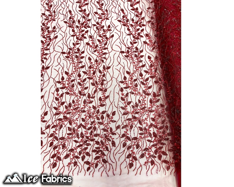 Puede incluir: Tela de encaje de color rojo burdeos con un patr&oacute;n floral. La tela tiene un acabado brillante y brillante.