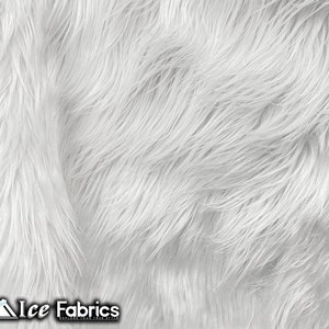 May include: Close-up of white faux fur fabric with long, flowing fibres. The fabric has a soft, textured appearance, with a slight sheen. The Ice Fabrics logo is visible in the bottom left corner.