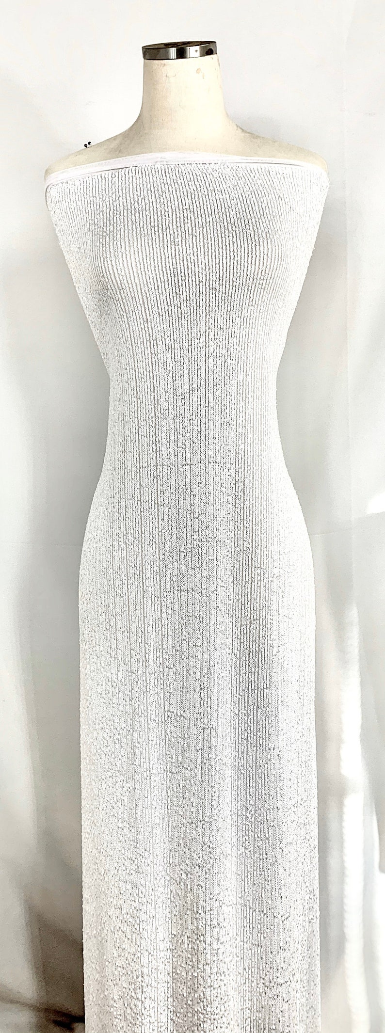 May include: White off-the-shoulder fabric with a textured, ribbed pattern. The fabric is draped over a white dress form.