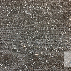 May include: Silver sequined fabric with a subtle shimmer. The sequins are small and closely packed together, creating a smooth and luxurious texture.