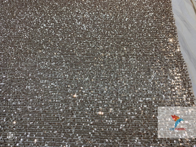 May include: Silver sequined fabric with a subtle shimmer. The sequins are small and closely packed together, creating a smooth and luxurious texture.