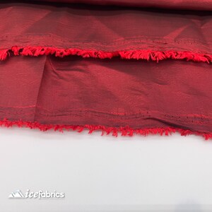 May include: Close-up of a deep red fabric with a slightly textured surface. The fabric has a raw edge with a frayed finish.