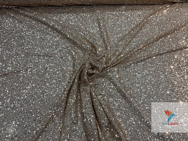 May include: A close-up of a silver sequined fabric with a brown undertone. The sequins are small and densely packed, creating a shimmering effect.