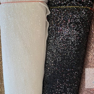 May include: Four rolls of sequined fabric in gold, white, black, and pink. The fabric is made of small, iridescent sequins.