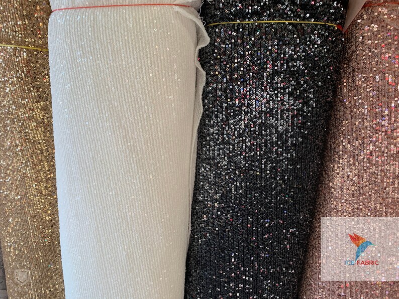 May include: Four rolls of sequined fabric in gold, white, black, and pink. The fabric is made of small, iridescent sequins.