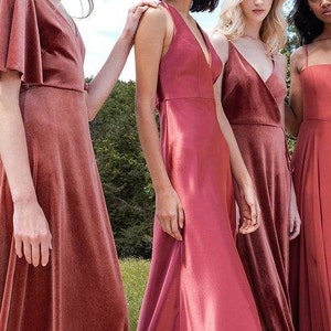 May include: Four women wearing different styles of long, rust-colored bridesmaid dresses. The dresses are all floor-length and have a variety of necklines and straps.