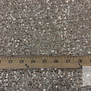 May include: Close-up of a gold sequined fabric with a ruler showing 20 inches. The sequins are small and evenly spaced.