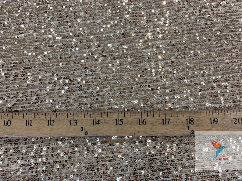 May include: Close-up of a gold sequined fabric with a ruler showing 20 inches. The sequins are small and evenly spaced.