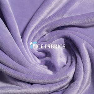 Könnte beinhalten: Ein weicher, hellvioletter Samtstoff mit dichter, plüschiger Textur, der in einem wirbelnden, drapierten Muster angeordnet ist. Der Stoff weist einen subtilen Glanz auf und ist mit dem weißen Text ICE FABRICS über den Falten versehen.