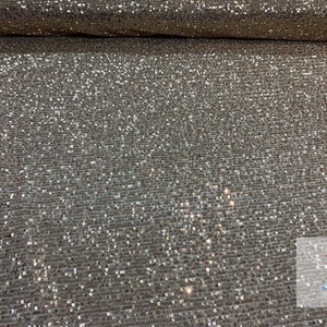 May include: Silver sequin fabric with a subtle shimmer. The fabric is woven with small, closely spaced sequins that create a sparkling effect.