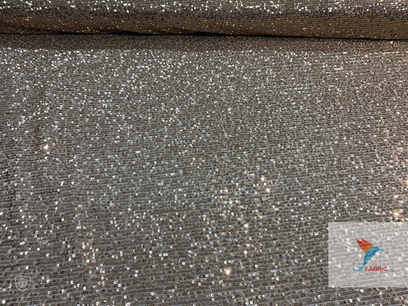 May include: Silver sequin fabric with a subtle shimmer. The fabric is woven with small, closely spaced sequins that create a sparkling effect.