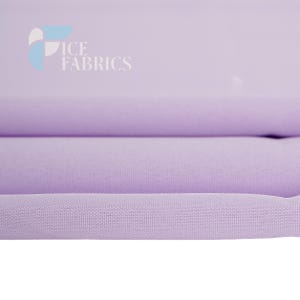 May include: A solid light purple fabric with a visible woven texture, folded into horizontal layers. The top left corner features a logo with the text ICE FABRICS in white letters, accompanied by a blue and white geometric graphic element.