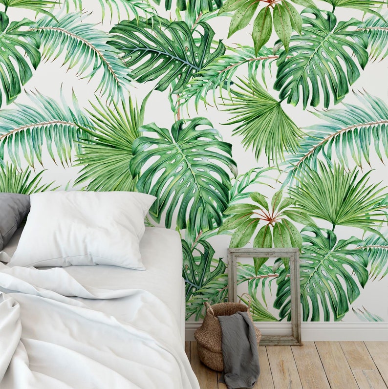 May include: A white wall with a tropical leaf wallpaper pattern. The wallpaper features large green leaves in a variety of shapes and sizes. A white bed with white bedding is in the foreground.
