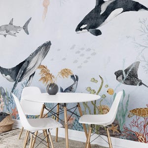 Pode incluir: Um mural de aquarela que apresenta uma variedade de criaturas marinhas, incluindo uma baleine, um tubarão, uma orca, uma arraia e uma tartaruga marinha. O mural é pintado em um fundo azul claro e inclui recifes de coral e algas marinhas. Uma mesa de jantar branca com quatro cadeiras está em primeiro plano.