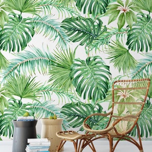 May include: A wicker chair and ottoman with a tropical leaf patterned wallpaper in the background. The chair has a high back and wide arms. The ottoman is a square shape with a woven top.