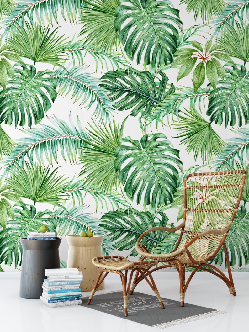 May include: A wicker chair and ottoman with a tropical leaf patterned wallpaper in the background. The chair has a high back and wide arms. The ottoman is a square shape with a woven top.