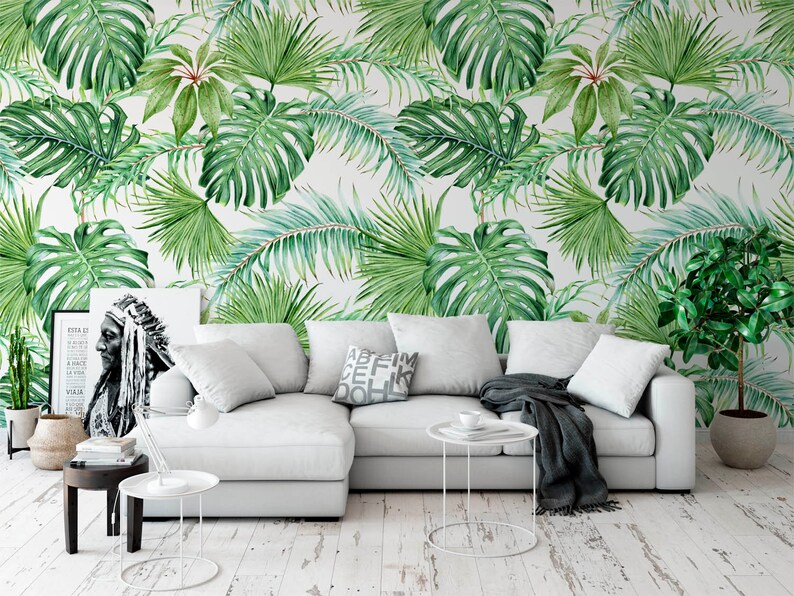 May include: A white sectional sofa with a gray throw blanket and a white side table with a cup on it. The sofa is in front of a wall with a tropical leaf wallpaper pattern.