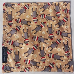 May include: Square fabric with a repeating pattern of sock monkey dolls in gray, red, and white on a tan background. White buttons are scattered throughout the design. The edges are stitched with dark thread.