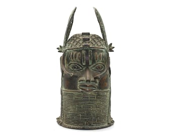 May include: A bronze sculpture of a human head with a crown and intricate details. The sculpture is green and brown in color and has a textured surface.