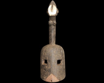 May include: A wooden mask with a tall, pointed top and two rectangular eye holes. The mask is dark brown and has a rough texture.
