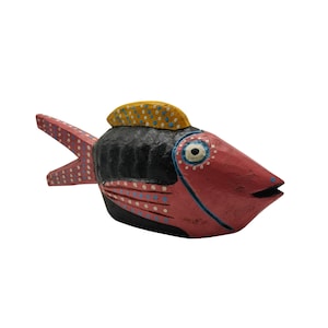 Puede incluir: Una figurita de pez de madera pintada a mano con pintura roja, negra, amarilla y blanca. El pez tiene un ojo grande y redondo y una pequeña aleta amarilla.