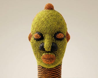 May include: A sculptural head covered in small beads. The face is primarily lime green with orange accents on the crown, ears, eyes, and mouth. The nose and eye sockets are dark brown. The neck features horizontal stripes of orange and dark brown beads.