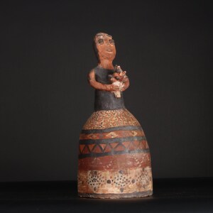 May include: A terracotta figurine of a woman holding a bouquet of flowers. The figurine is painted in black, brown, and white with geometric patterns.