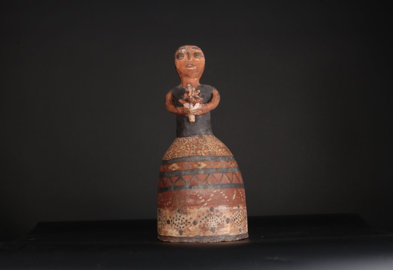 May include: A ceramic figurine of a person wearing a black and brown dress with geometric patterns. The figurine is holding a bouquet of flowers in its hands.