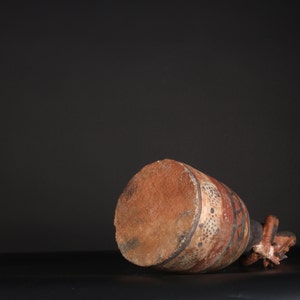 May include: A brown ceramic pot with a geometric design in black, white, and red. The pot is lying on its side, revealing the bottom.