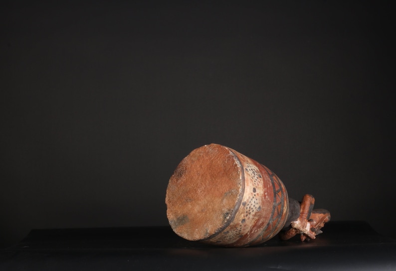 May include: A brown ceramic pot with a geometric design in black, white, and red. The pot is lying on its side, revealing the bottom.