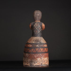 May include: A ceramic figurine of a person with a brown and black painted design. The figurine is wearing a skirt with geometric patterns in brown, black, and white.