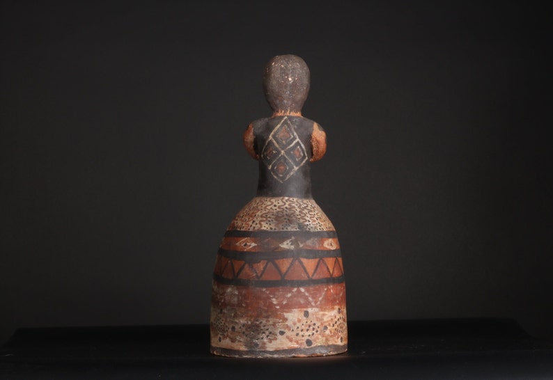 May include: A ceramic figurine of a person with a brown and black painted design. The figurine is wearing a skirt with geometric patterns in brown, black, and white.
