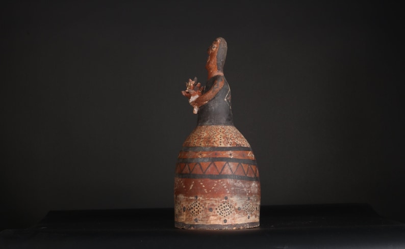 May include: A ceramic figurine of a person with a black and brown painted design. The figurine is standing on a black surface.