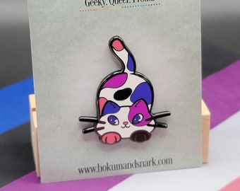 May include: A colourful enamel pin featuring a cartoon cat with pink, blue and white fur. The cat is sitting on its hind legs with its tail raised. The pin is on a card with the text "Hokum and Snark" and "Geeky. Queer. Proud." The card also includes the website address "www.hokumandsnark.com".