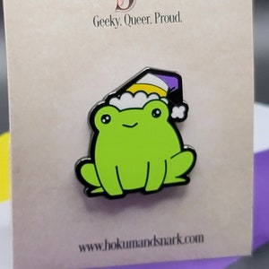 May include: A green frog wearing a purple, yellow and white hat with the text "Hokum and Snark, Geeky. Queer. Proud." and the website "www.hokumandsnark.com" on a white background.