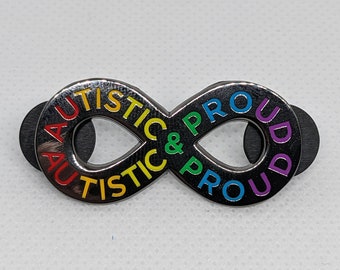 May include: A silver infinity symbol pin with the words "Autistic & Proud" written around it in rainbow colors.