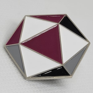 May include: A silver-toned pin with a geometric design. The pin is shaped like a hexagon and features a white, gray, black, and burgundy color scheme.