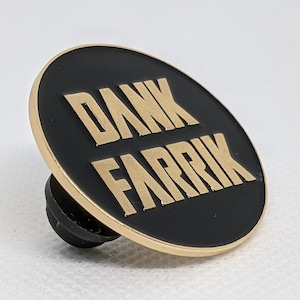 May include: A black and gold round pin with the text "DANK FARRIK" in gold letters.
