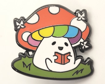 May include: A white mushroom character with a rainbow cap sits on a green patch of grass and reads a red book. The mushroom has a happy face and is wearing a red and white spotted cap.