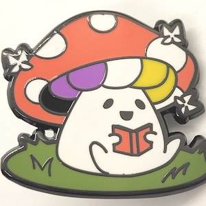 May include: A colorful enamel pin featuring a cartoon mushroom with a purple, yellow, and white cap. The mushroom is wearing a white dress and holding a red book. The mushroom is sitting on a green patch of grass.