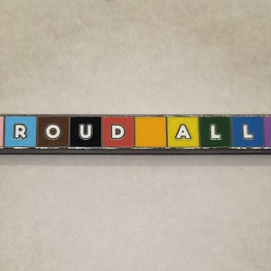 May include: A rainbow-coloured enamel pin spelling out the word "PROUDLY".