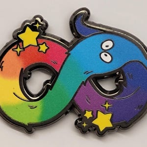 May include: Rainbow coloured enamel pin featuring a cartoon worm with two eyes, forming an infinity symbol. The worm is surrounded by yellow stars with sparkles.